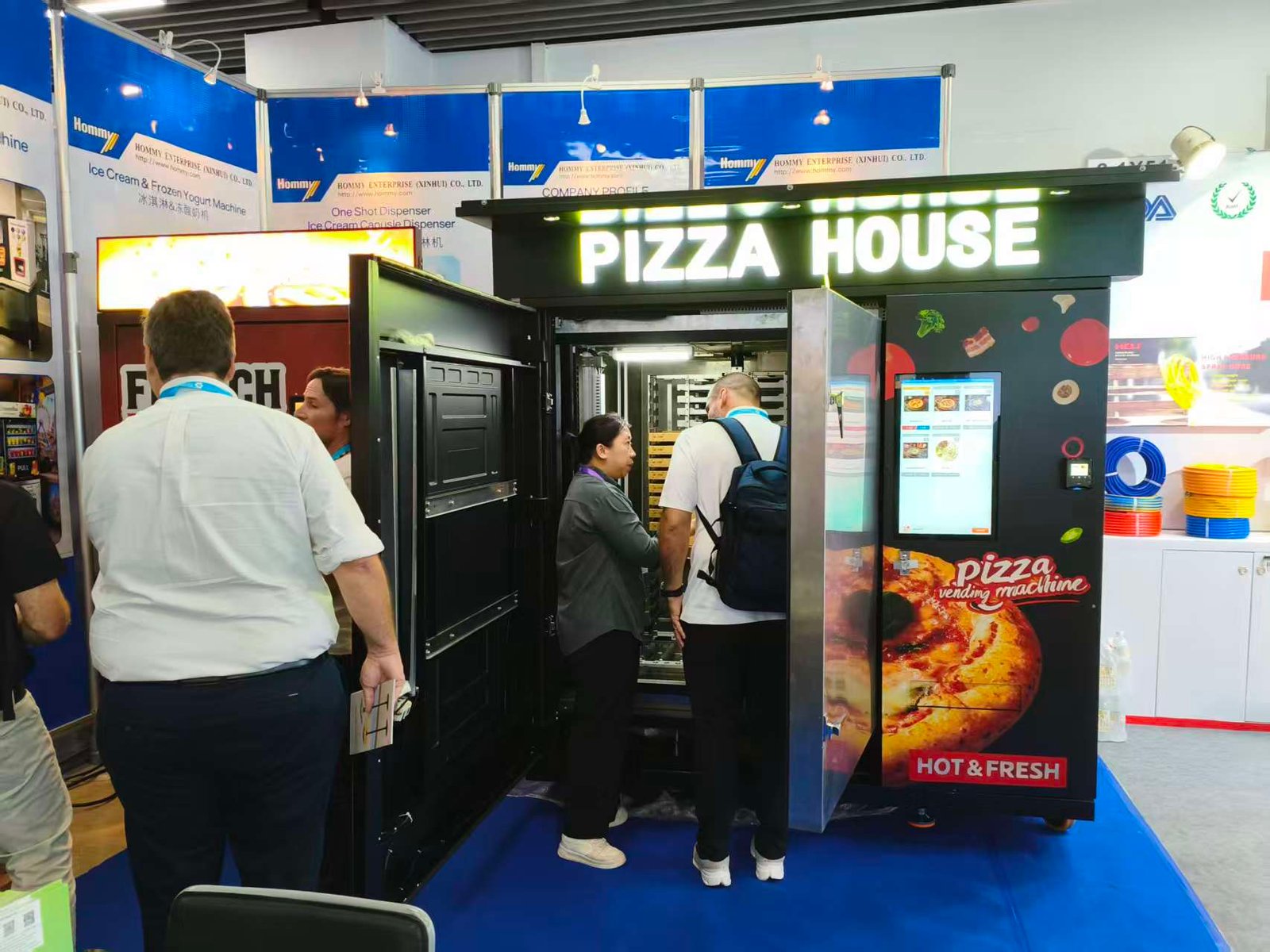 Staff demonstrating the open compartments of the Pizza House machine to overseas clients